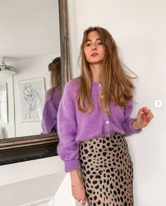 a woman standing in front of a mirror wearing a purple sweater and leopard print skirt