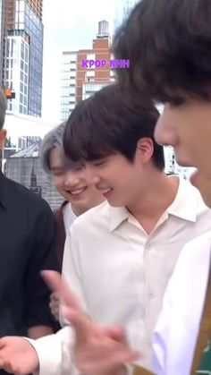 two men are talking to each other in front of some buildings and one man is wearing a black shirt