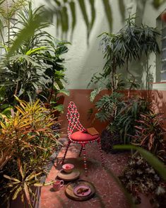 a red chair sitting on top of a brick walkway next to lots of trees and plants