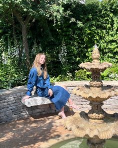 a woman sitting on a stone bench next to a fountain