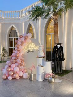 a cake and balloons are on display in front of a white building with palm trees