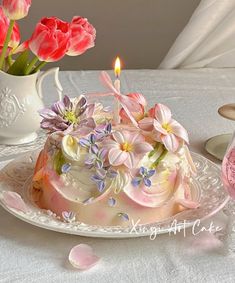 there is a cake with flowers on it and a candle in the middle, next to some pink tulips