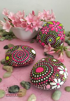 three painted rocks sitting on top of a pink table