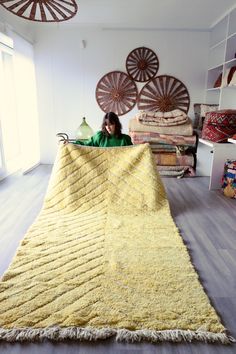 a woman sitting on the floor in front of a large rug that has been made with yarn