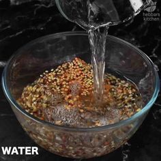 water being poured into a glass bowl filled with grains and seeds on a black marble counter top