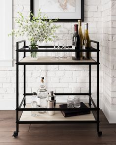 a bar cart with bottles and glasses on it in front of a white brick wall