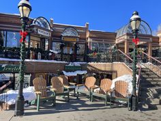 several wooden chairs and tables in front of a building with snow on the ground around them