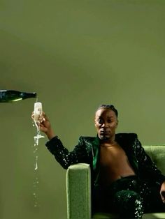 a man sitting on a green couch with a bottle and glass in his hand as he pours champagne