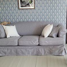 a gray couch sitting in front of a blue wall with white pillows on top of it