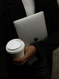 a man in a suit holding a coffee cup and an apple laptop