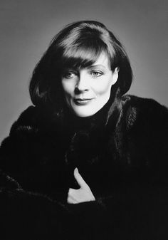 black and white photograph of woman in fur coat with hand on chest, looking at camera