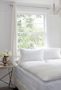 a bed with white sheets and pillows in front of a window