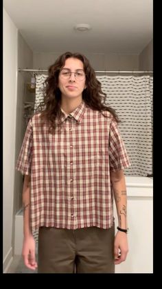 a man with long hair and glasses standing in front of a mirror wearing a plaid shirt