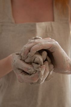 a woman is holding out her hands covered in clay