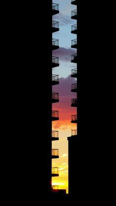 a tall building with balconies against a colorful sunset in the background at dusk