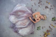 a woman in a purple dress laying on the ground with her hands behind her back