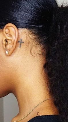 the back of a woman's head with a cross tattoo on her left ear