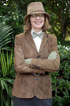 a woman wearing a brown jacket and hat with her arms crossed