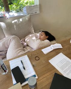 a woman laying on top of a wooden table next to a bottle of water and papers