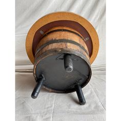 an old wooden barrel sitting on top of a white cloth covered table next to a metal pipe