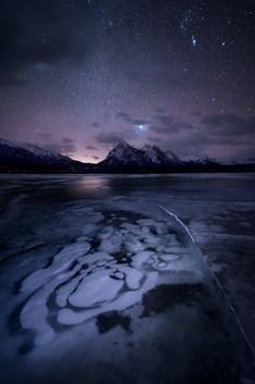 the night sky is lit up with stars above water and snow covered mountains in the distance