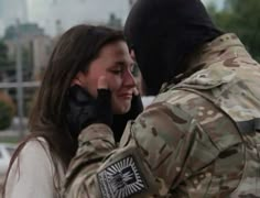 a soldier is talking on the phone with a woman in uniform and holding her arm around him