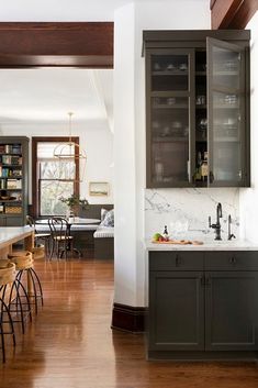 an open kitchen and dining room with wood flooring, white walls and dark gray cabinets