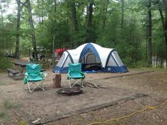 two lawn chairs sitting in front of a blue and white tent next to a fire pit