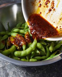 a bowl filled with green beans and sauce being poured on top of the food in it