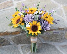 a bouquet of sunflowers and other flowers is sitting on the stone floor next to a brick wall