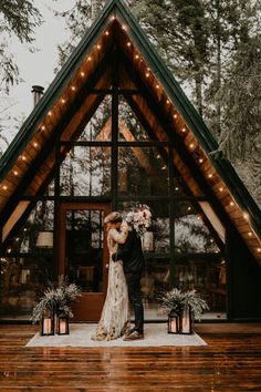 a bride and groom standing in front of a wooden cabin with lights on the roof