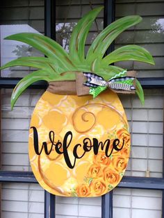 a welcome pineapple door hanger with flowers on the front and side, hanging from a window