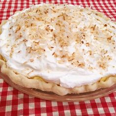 a pie with coconut on top sitting on a red and white checkered table cloth