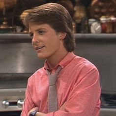 a young man wearing a pink shirt and tie standing in front of an oven with his arms crossed