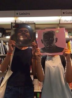 two people holding up posters in front of bookshelves, one with a man's face on it