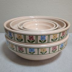 three bowls are stacked on top of each other, with flowers painted on the sides