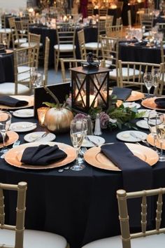 the tables are set with black linens, gold chargers and pumpkins for centerpieces