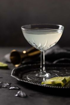 a glass filled with white liquid and lime slices on a black serving tray next to a bottle