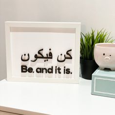 a white framed sign that says be and it is next to a potted plant