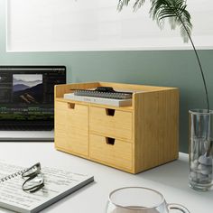 an open laptop computer sitting on top of a white desk next to a wooden drawer