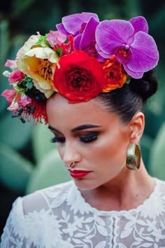 a woman with flowers in her hair is wearing earrings and a white top that has red, yellow, pink, orange and purple flowers on it