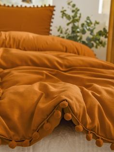 an orange comforter with pom - poms on the bottom is laying on a bed