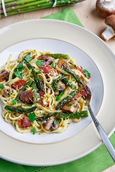 a white plate topped with pasta and asparagus on top of a wooden table