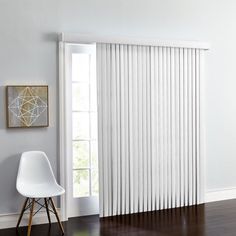 a white chair sitting in front of a window with vertical blinds on the windowsill