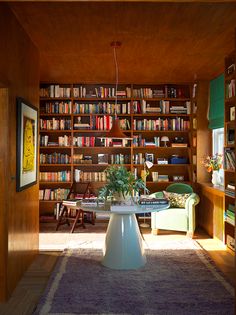 a living room with bookshelves full of books and plants on the table in front of it