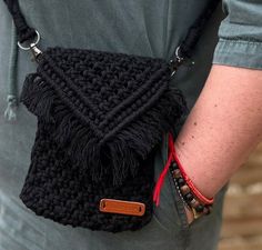 a black crocheted bag with red string and tassels is held by a man's arm