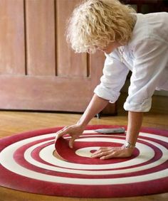 a woman is bending over to pick up the red and white rug on the floor