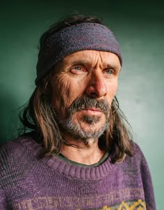 a man with long hair wearing a purple sweater and a headband is looking at the camera