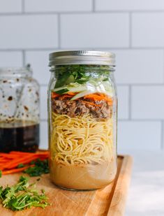 a mason jar filled with noodles, meat and veggies on a cutting board