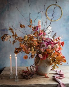 a vase filled with lots of flowers next to two candles